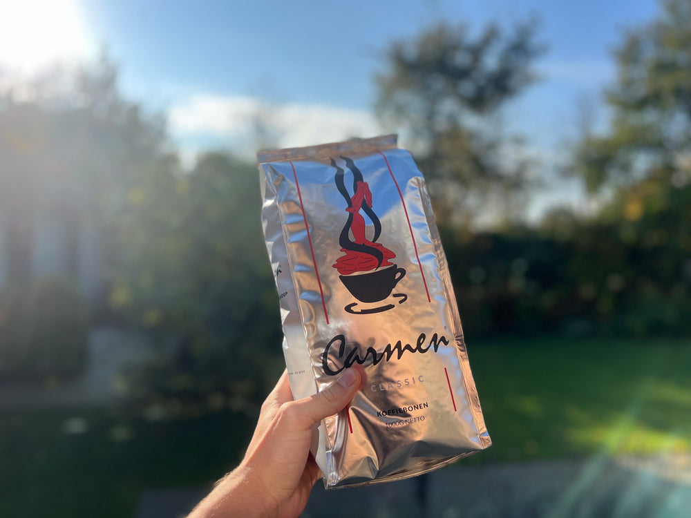 Zak Carmen Classic koffiebonen van 1000g, vastgehouden in het zonlicht met een natuurlijke achtergrond. Premium kwaliteit koffie van CaféHuis, perfect voor liefhebbers van een klassieke en rijke smaakbeleving.